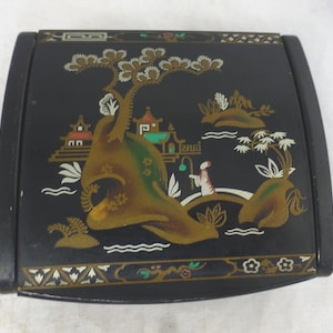 Puede incluir: Caja de madera lacada en negro con tapa con bisagras. La tapa presenta un diseño de inspiración asiática colorido con una escena de paisaje dorada, verde y blanca. La caja tiene un borde decorativo alrededor del borde.