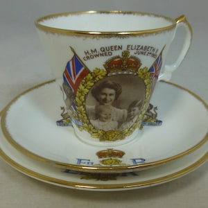 Op de afbeelding: Een wit theeservies met een gouden rand. De theekop heeft een portret van koningin Elizabeth II en de tekst "H.M. QUEEN ELIZABETH II CROWNED JUNE 2ND 1953". De schotel heeft de tekst "E.R." met een kroon.