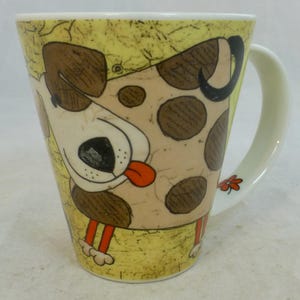 Peut inclure: Une grande tasse en céramique avec un dessin de chien de dessin animé. Le chien a des taches marron, un visage beige et une langue rouge. La tasse a un fond jaune avec un aspect texturé et une anse blanche.