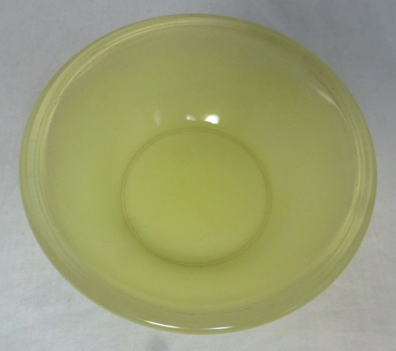May include: A pale yellow glass bowl with a smooth, rounded rim. The bowl is empty and has a slight sheen.