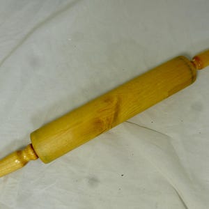 May include: A wooden rolling pin with a light brown color and a slightly textured surface. The rolling pin has a handle on each end.
