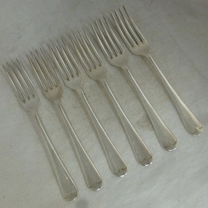 May include: Six silver forks with ornate handles. The forks are arranged in a row, with the handles pointing to the right.