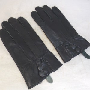 May include: A pair of black leather gloves with a button closure on the wrist. The gloves have a green lining.