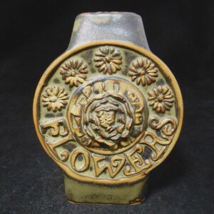 May include: A green ceramic vase with a brown floral design and the word "FLOWERS" embossed on the front.