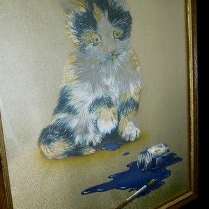 Puede incluir: Una pintura enmarcada de un gatito calico sentado sobre un fondo dorado con un frasco de pintura azul derramado y un pincel.