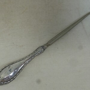 Puede incluir: Un calzador de plata con un mango adornado. El mango está decorado con un patrón floral. El calzador es largo y delgado.