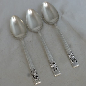 Puede incluir: Tres cucharas de plata con diseños florales ornamentados en los mangos.