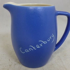 May include: A blue ceramic pitcher with a white handle and the word "Canterbury" written on the side in white.