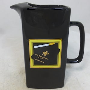 May include: Black ceramic jug with a gold and yellow John Player Special cigarette pack design. The pack has a white cigarette sticking out of it.