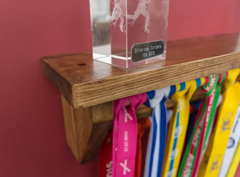 May include: A wooden shelf with a clear glass trophy on top. The trophy has a silver plaque that reads "Billericay Striders 10k 2010". The shelf is decorated with colorful ribbons.
