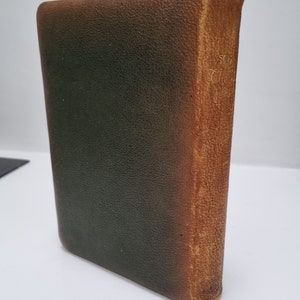 K&ouml;nnte beinhalten: Ein Vintage-Buch mit Lederbindung, dunkelgr&uuml;nem Einband und braunem R&uuml;cken. Der R&uuml;cken tr&auml;gt den Text "The" und einen weiteren Text, der nicht sichtbar ist.