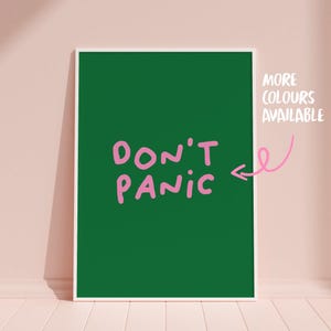 Könnte beinhalten: Ein gerahmter Kunstdruck mit dunkelgrünem Hintergrund und den Worten "DON'T PANIC" in rosa Schrift. Der Satz ist auf dem Druck zentriert. Die Worte "MORE COLOURS AVAILABLE" stehen in weißem Text in der oberen rechten Ecke.