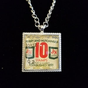 May include: A silver chain necklace with a square pendant featuring a vintage Green Stamps advertisement. The pendant has a white background with red text that reads "10 Stamps" and "Value 10 2/3 Mills". The text "Established 1896" is also visible.
