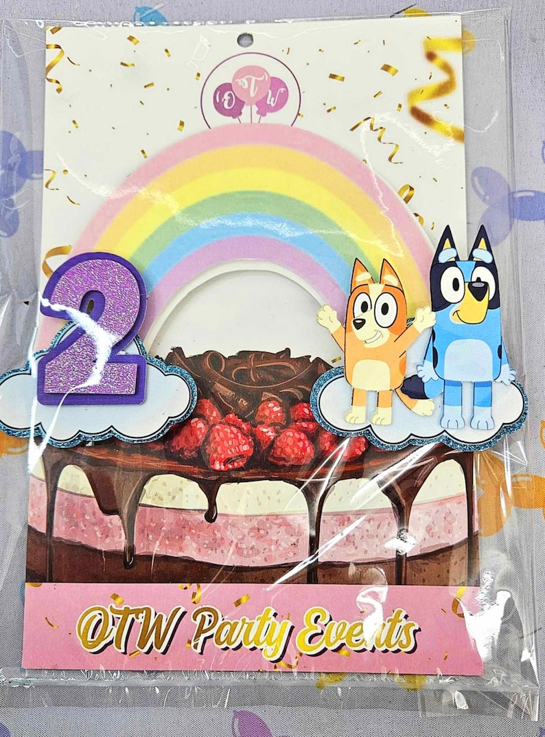 Puede incluir: Un conjunto de adornos para tartas con un arco&iacute;ris, dos perros de dibujos animados y un n&uacute;mero 2 morado. Los perros son del programa Bluey. El adorno est&aacute; sobre una tarta rosa y marr&oacute;n con chocolate y frambuesas. El texto "OTW Party Events" est&aacute; en la parte inferior de la imagen.