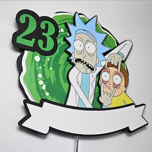 May include: A colorful cake topper featuring cartoon characters Rick and Morty, with the number 23 in green. The background is a green portal design, and a white banner is at the bottom.