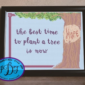 May include: Cross stitch pattern featuring a tree with the words "the best time to plant a tree is now" and "Hope" carved into the trunk. The pattern is framed and ready to be stitched.