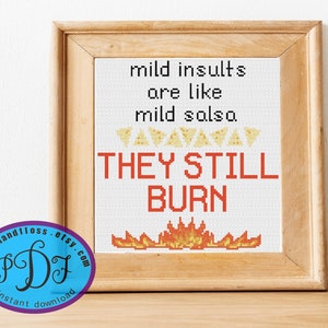 May include: Cross-stitch art in a wooden frame with the text "mild insults are like mild salsa. THEY STILL BURN." The design includes images of tortilla chips and flames. A logo for "stitchandfloss.etsy.com" is in the lower left corner.