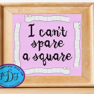 May include: A pink cross-stitch pattern with the text "I can't spare a square" in black. The pattern is surrounded by a white border and a wooden frame.