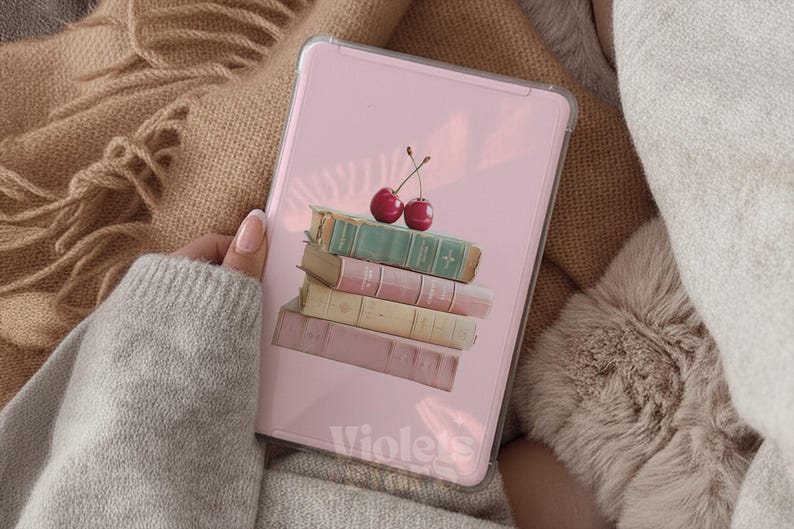 Pu&ograve; includere: Una custodia rettangolare per tablet con sfondo rosa chiaro che presenta una pila di quattro libri nelle tonalit&agrave; verde, rosa, crema e malva, sormontata da due ciliegie rosse. La parola Violets &egrave; stampata in bianco nella parte inferiore.