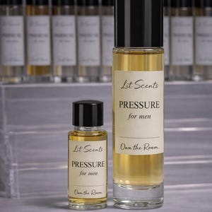 May include: Two glass perfume bottles with black caps, one tall and one small, filled with a golden liquid. The labels read "Lit Scents PRESSURE for men" and "Own the Room."
