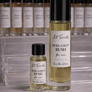 May include: Two glass perfume bottles with black caps, one large and one small, labeled "Lit Scents BERGAMOT RUSH for men." The background features a row of similar bottles. The text "Own the Room" is also visible.