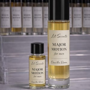 May include: Two glass perfume bottles with black caps and labels that read "Lit Scents MAJOR MOTION for men." The bottles are filled with a golden liquid. The text "Own the Room" is also visible.