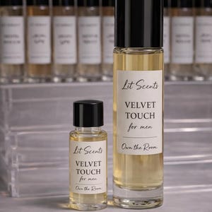 May include: Two perfume bottles with black caps and clear glass, one large and one small, are displayed. The bottles have white labels with the text "Lit Scents VELVET TOUCH for men Own the Room." Additional bottles are in the background.
