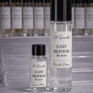 May include: Two clear glass perfume bottles with black caps. The larger bottle has a label that reads "Lit Scents EASY MOTION for men Own the Room." The smaller bottle has the same label. Additional bottles are in the background.