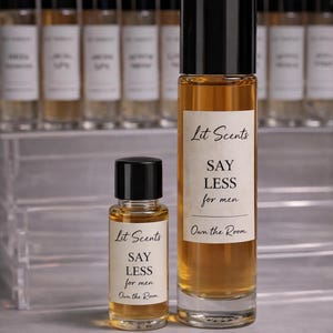 May include: Two amber-colored perfume bottles with black caps, labeled "Lit Scents" and "SAY LESS for men." A smaller bottle is in front of a larger one. The background features additional perfume bottles.