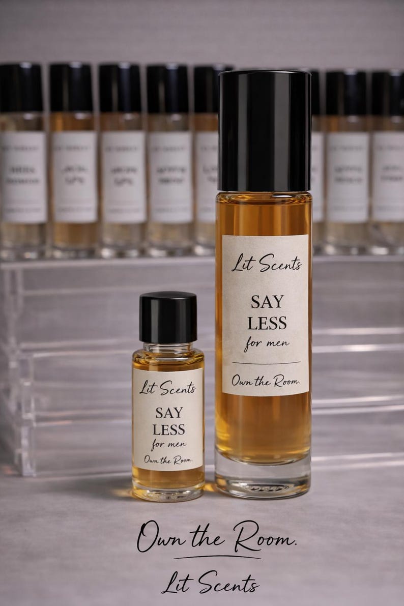 May include: Two amber-colored perfume bottles with black caps, labeled "Lit Scents" and "SAY LESS for men." A smaller bottle is in front of a larger one. The background features additional perfume bottles.