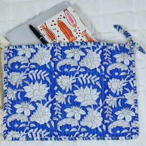May include: A rectangular quilted fabric sleeve featuring a vibrant blue background with a repeating white floral and leaf pattern. The sleeve has a matching blue fabric tie closure on the right side and contains a white notebook with orange fish.