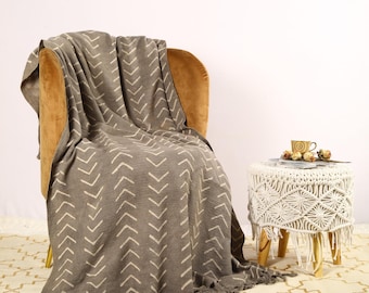 May include: A gray throw blanket with a white chevron pattern draped over a brown armchair. The blanket has fringe on the edges.