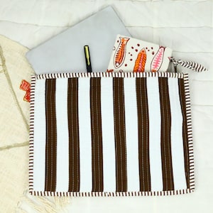 May include: A rectangular quilted pouch featuring vertical brown and white stripes with a matching striped border. Inside the pouch are a grey laptop, a black pen, and a white wallet decorated with a colourful orange and pink fish pattern.