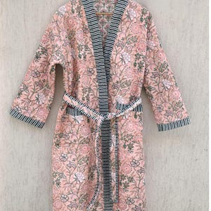 May include: A pink floral print robe with a black and white striped trim. The robe has a tie belt and long sleeves.