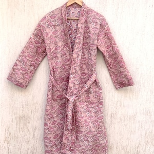 Puede incluir: Una bata de color rosa y blanco con estampado floral y cinturón de lazo. La bata está hecha de una tela suave y ligera y tiene un corte holgado.