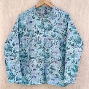 Op de afbeelding: Een lichtblauw gewatteerd jack met een bloemenprint. Het jack heeft een mandarijnskraag en een knoopsluiting.