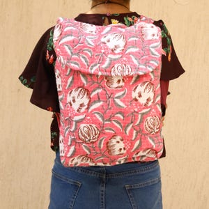 Op de afbeelding: Een roze en witte rugzak met een bloemenpatroon en een klep. De rugzak is gemaakt van een gestikt materiaal.