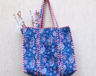 May include: A blue tote bag with a floral print and red and white trim. The bag has two straps and is made of quilted fabric.