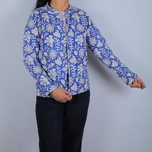 Könnte beinhalten: Blaue Jacke mit weißem Blumenmuster. Die Jacke hat lange Ärmel und einen Stehkragen. Das florale Design bedeckt die gesamte Jacke. Die Jacke ist vorne offen.