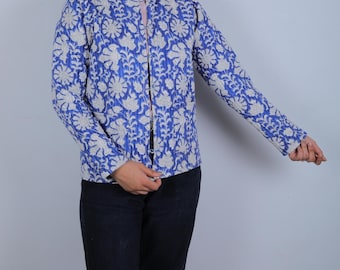 May include: A blue jacket with a white floral pattern. The jacket has long sleeves and a mandarin collar. The floral design covers the entire jacket. The jacket is open in the front.
