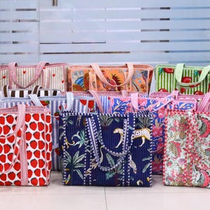 May include: A collection of rectangular quilted tote bags featuring various patterns including red strawberries, blue jungle prints with leopards, green striped fruit designs, and floral motifs, all equipped with matching fabric handles.