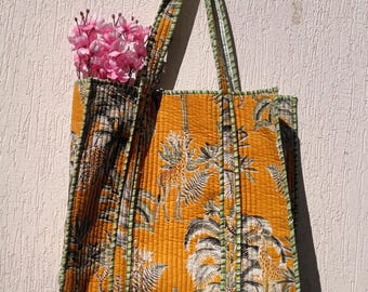 Può includere: Borsa tote trapuntata con sfondo giallo vibrante e stampa a tema safari con giraffe e palme. La borsa ha finiture e manici verdi ed è piena di fiori rosa. La borsa misura circa 38 cm di larghezza e 41 cm di altezza.