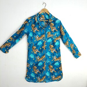 Peut inclure: Une chemise bleue à manches longues avec un devant boutonné et un imprimé tigre. La chemise a une bordure jaune autour du col et des poignets.
