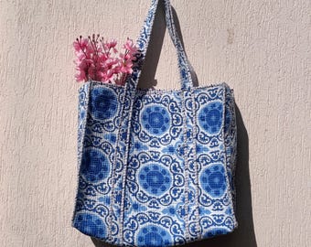 Può includere: Una borsa tote blu e bianca con un motivo floreale. La borsa ha due manici ed è realizzata in tessuto intrecciato.