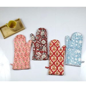 May include: Four colorful quilted oven mitts with floral and geometric patterns. The mitts are in shades of pink, red, blue, and white.