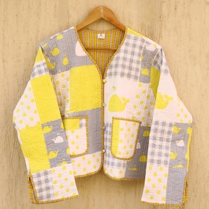 Könnte beinhalten: Eine gelbe und graue gesteppte Jacke mit Patchwork-Muster mit Walen und Punkten. Die Jacke hat einen V-Ausschnitt, lange Ärmel und zwei Taschen. Das Größenetikett zeigt "XL".