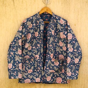 Pode incluir: Casaco acolchoado azul marinho com um padrão floral em tons de rosa e branco. O casaco tem gola mandarim e dois bolsos. Está pendurado num cabide de madeira. O desenho floral é repetido por todo o casaco.