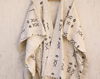 May include: A white cotton poncho with a black and white geometric pattern. The poncho has fringe along the bottom edge.