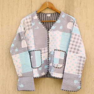 May include: A gray and blue quilted jacket with a patchwork design featuring whales, polka dots, and gingham patterns. The jacket has a V-neck, button closure, and two patch pockets.