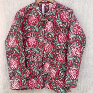 Puede incluir: Una chaqueta acolchada roja con estampado de piña verde y blanca. La chaqueta tiene un cuello mandarín y cierre de botón.
